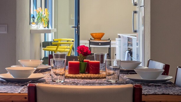 Un comedor con una mesa dispuesta para cuatro, que incluye platos, vasos y un jarrón con flores.