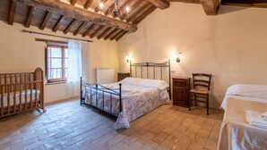Ein Schlafzimmer mit Holzboden, einem Metallbettgestell, einem Holzstuhl, einem Nachttisch und einem Fenster mit Vorhängen.