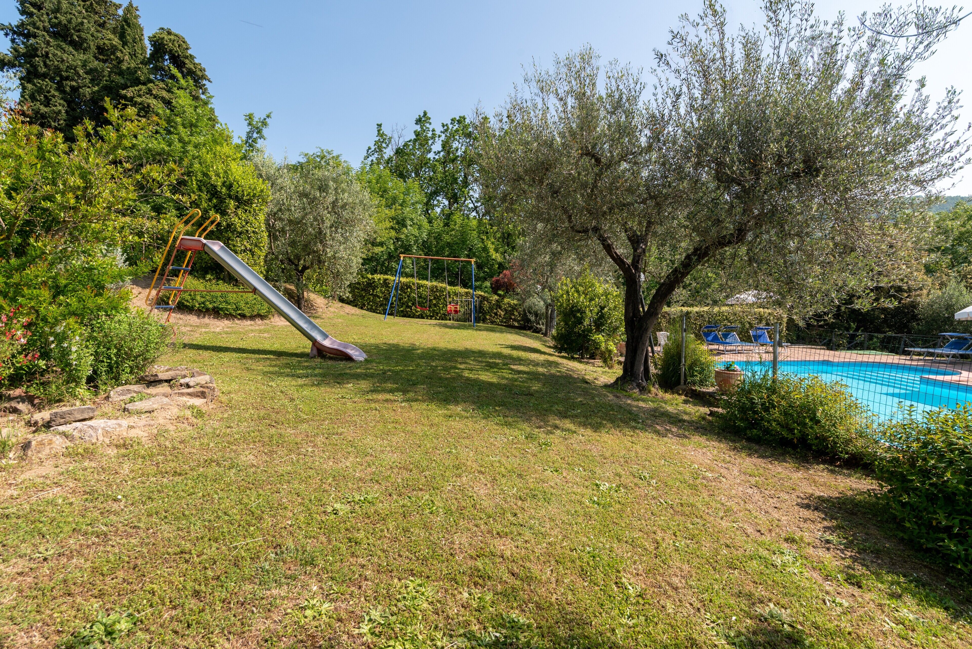 Un espacio con césped, un tobogán, una piscina y árboles.