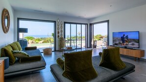 Un salon moderne doté d’un grand téléviseur, de sièges confortables et offrant une vue sur l’extérieur.