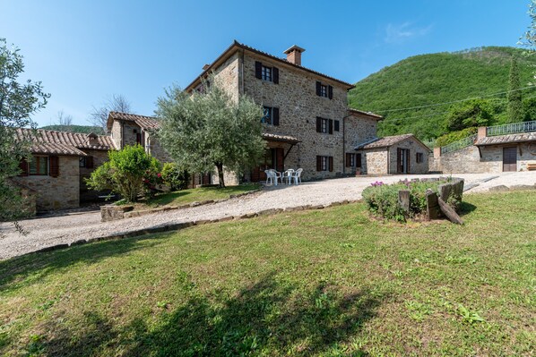 Un bâtiment en pierre doté d’une cour, d’un petit jardin et offrant une vue sur une colline.