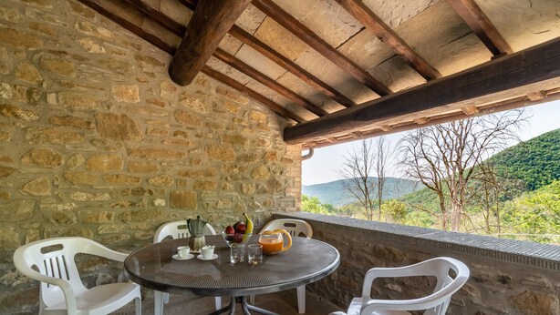 A stone wall, a round table with chairs, a bowl of fruit, and a glass of juice.