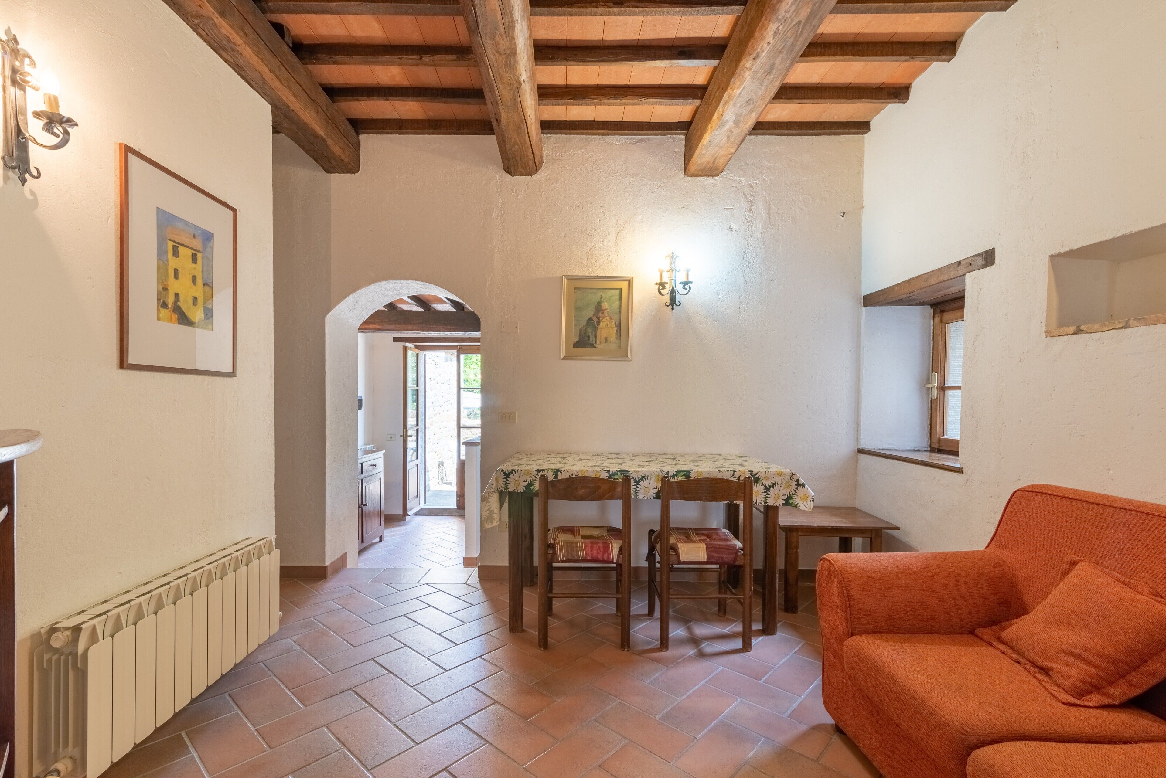 A room with a wooden ceiling, a radiator, a table with chairs, and an orange sofa.