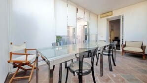 Zona de menjador moderna amb taula de vidre, cadires negres i un sofà de vimetina.