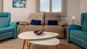 Un soggiorno moderno con poltrone color petrolio, un divano beige con una coperta decorata e un tavolino da caffè bianco con una ciotola nera.