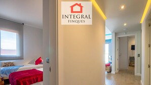 Una camera d'albergo moderna con un letto, un comodino e una finestra. Sul muro è presente un cartello con la scritta "INTEGRAL FINQUES".
