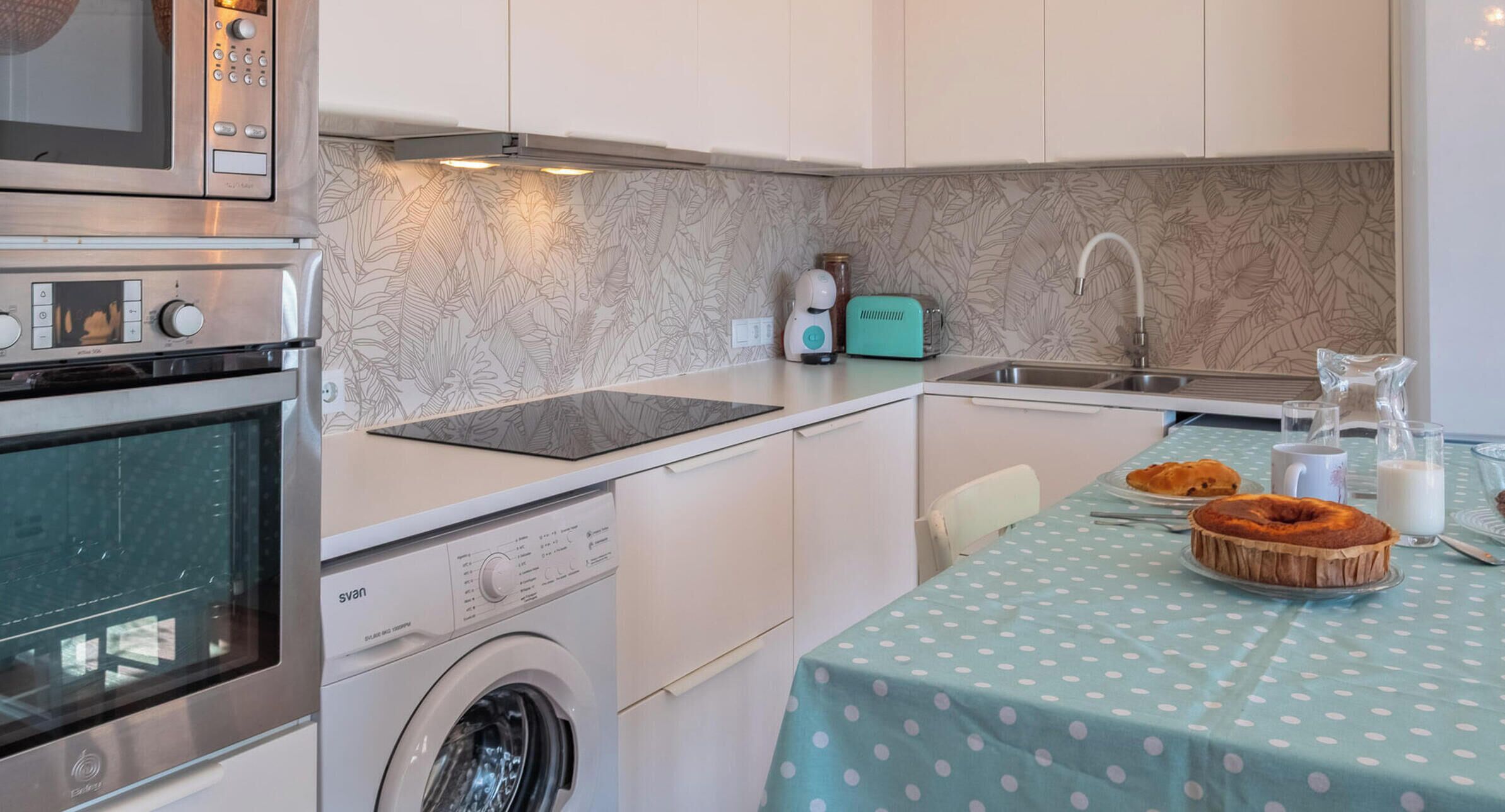 Uma cozinha compacta com máquina de lavar, micro-ondas, torradeira e pia.