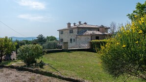 Ein Haus aus Stein mit einem Ziegeldach, umgeben von einem grünen Rasen und blühenden Sträuchern.
