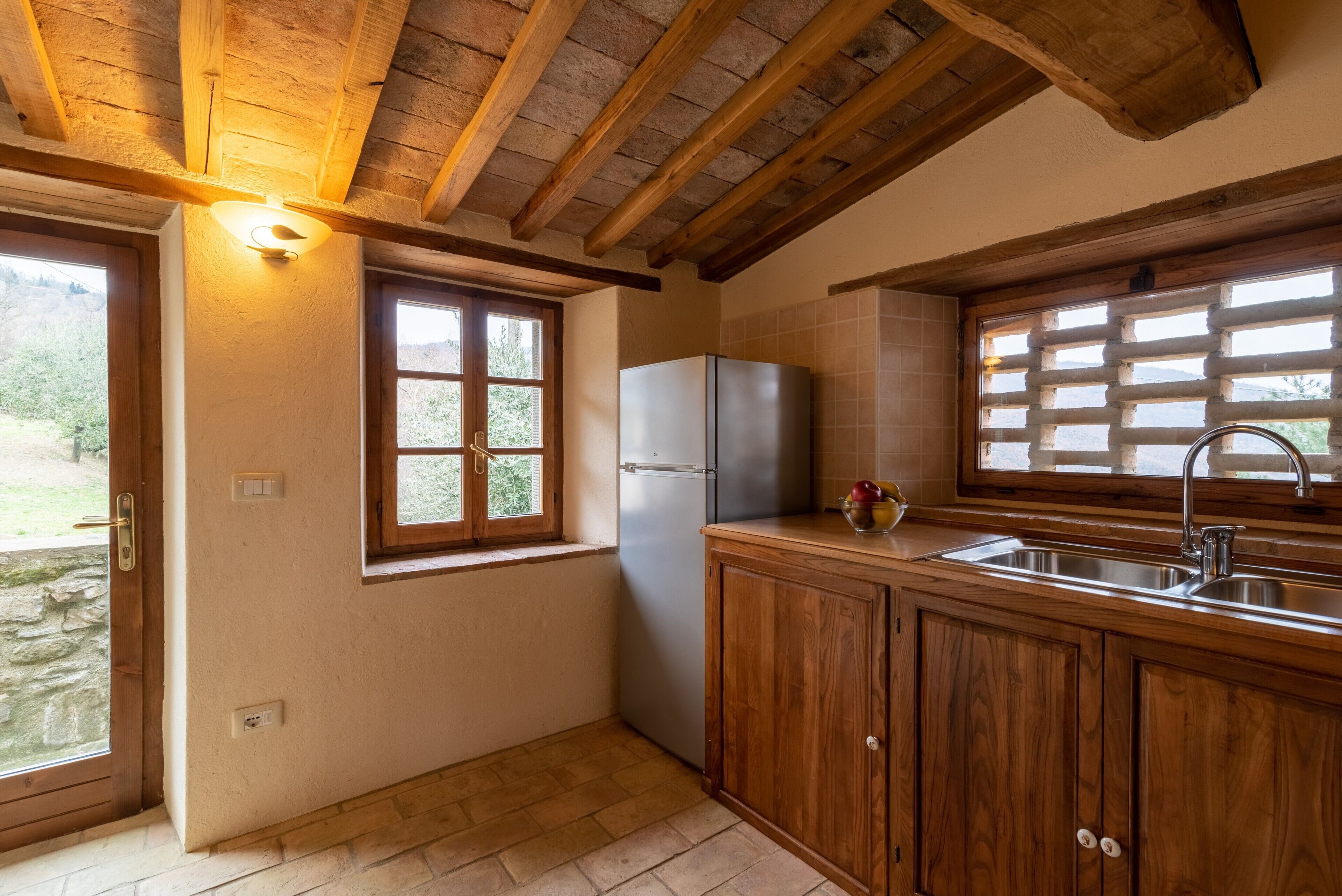 Una cocina con armarios de madera, un refrigerador, un lavamanos y una ventana con persianas.
