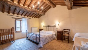 Una camera da letto con soffitto in legno, un letto, una sedia, un comodino e una finestra.