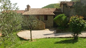 Un edificio in pietra con tetto in tegole, circondato da un cortile in ghiaia e da piante.
