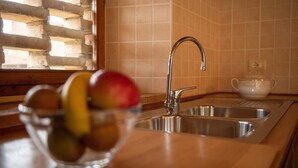 Una cucina con un lavello in acciaio inossidabile, una ciotola di frutta e una finestra con persiane.