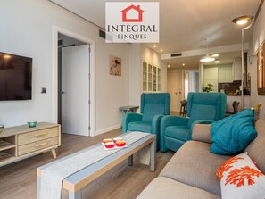 A modern living room with teal armchairs, a grey sofa, and a wooden coffee table with red bowls.