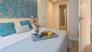 A neatly made bed with a tray of breakfast items, a bedside table with a lamp, and a bathroom visible through an open door. - Modern Apartment, 2 Bedrooms, 150m from Beach, Central Palamós, with Parking, WiFi & A/C (Palamós)