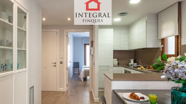 A modern kitchen with a dining area, a visible door leading to another room, and a logo for 'Integral Finques'. - Modern Apartment, 2 Bedrooms, 150m from Beach, Central Palamós, with Parking, WiFi & A/C (Palamós)