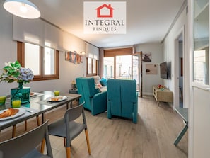 A modern living room with teal chairs, a dining table with breakfast items, and a large window.