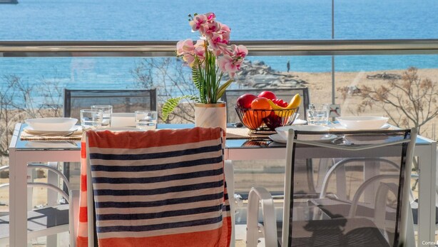 Una mesa de comedor con vista al océano, un frutero y una toalla rayada en una silla.