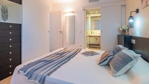 Una habitación de hotel con cama, mesita de noche, cómoda y baño visible a través de una puerta abierta.