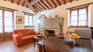 A cozy living room with a fireplace, a dining table with food, a sofa, and a laptop. - Agriturismo 'Cuiano La Loggetta' with Shared Pool, Garden and Wi-Fi (Cortona)