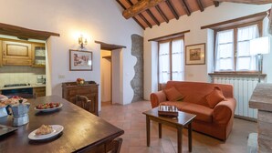 A cozy living area with a wooden table, sofa, and a stone accent wall. - Agriturismo 'Cuiano La Loggetta' with Shared Pool, Garden and Wi-Fi (Cortona)