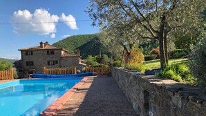 A swimming pool with a stone wall and a wooden fence, a stone building with a tiled roof, and a mountainous landscape in the background. - Agriturismo 'Cuiano La Loggetta' with Shared Pool, Garden and Wi-Fi (Cortona)