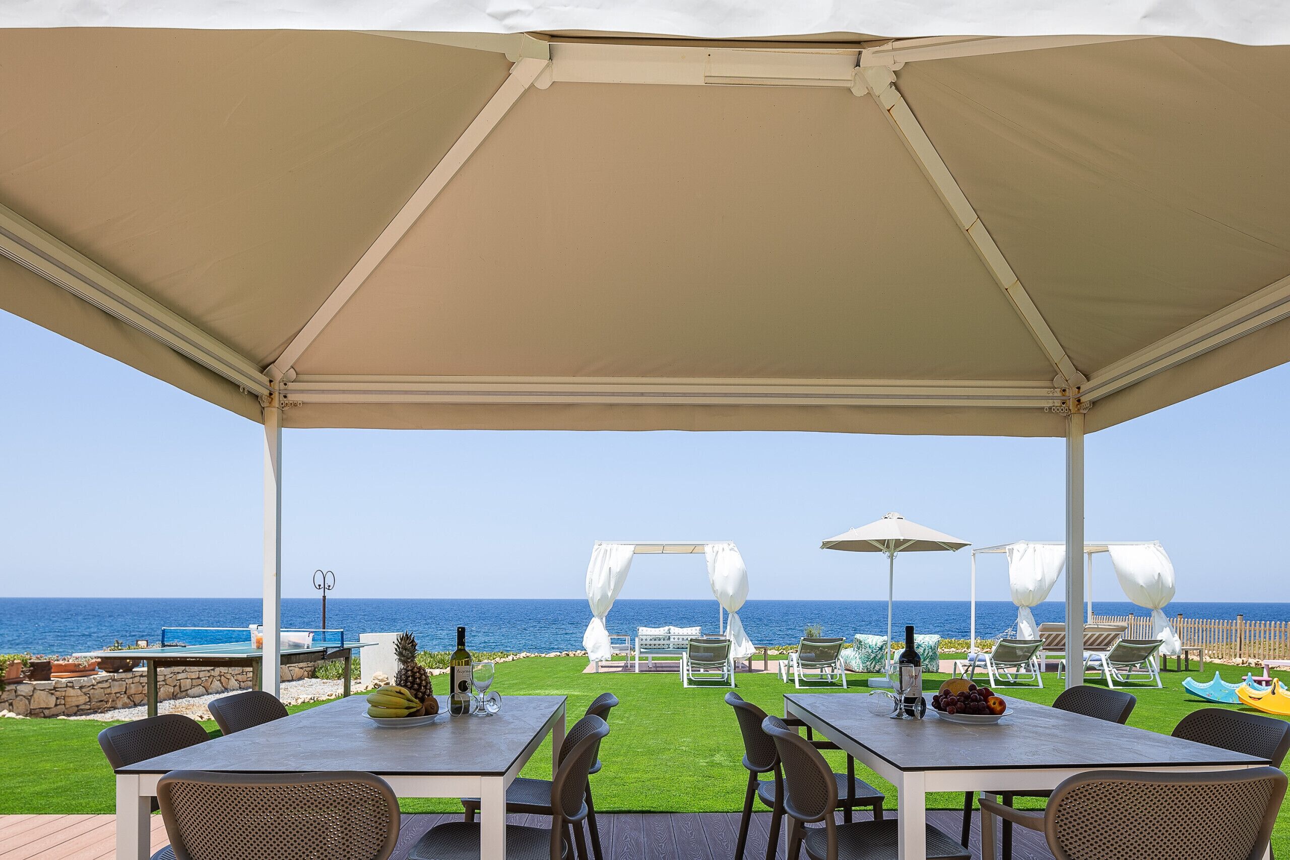 An outdoor patio with a table and chairs, a white canopy, and a view of the ocean.