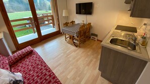 A compact living space with a dining area, a kitchenette, and a sliding glass door leading to a garden.