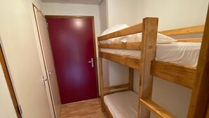 A narrow hallway with a wooden bunk bed and a red door.