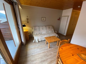 A cozy room with a wooden floor, a bed with patterned bedding, a small wooden table, and a chair.