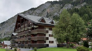 Un immeuble à plusieurs étages, doté de balcons, qui se dresse sur un fond de paysage montagneux.