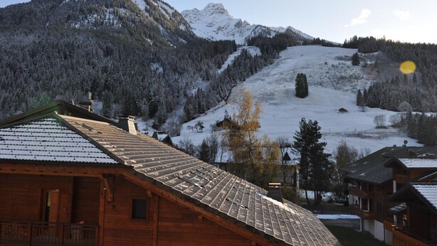 Une cabane en bois, dotée d’un toit en pente, entourée de montagnes et d’arbres couverts de neige.