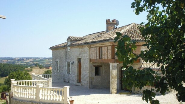 A stone building with a tiled roof, a gravel driveway, and a white fence.