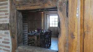 A rustic dining area with wooden tables and chairs, a brick wall, and a large wooden door.