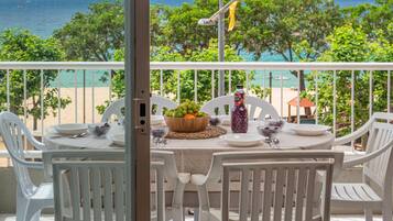 Mesa para dos personas con sillas blancas, un frutero, una botella de jugo y vistas a la playa y al océano.