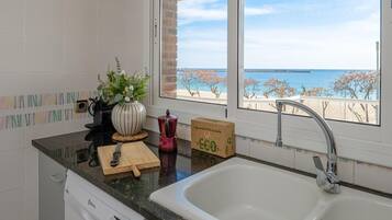 Una cocina con vistas a la playa, un lavabo, una tabla de cortar, un cuchillo, una planta y una caja de toallas de papel ecológicas.