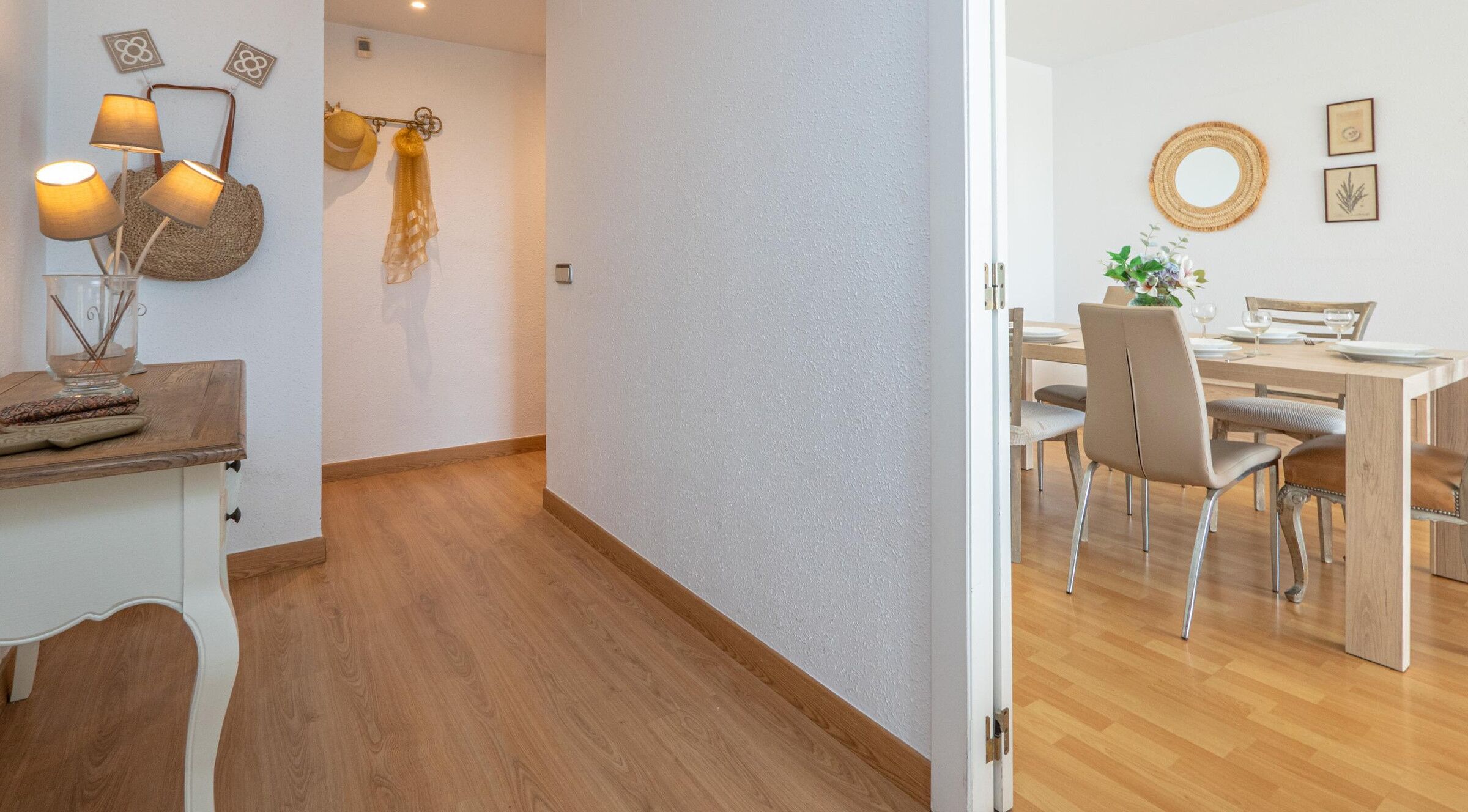 A hallway leading to a dining area with a wooden floor, a table set for two, and a chair.
