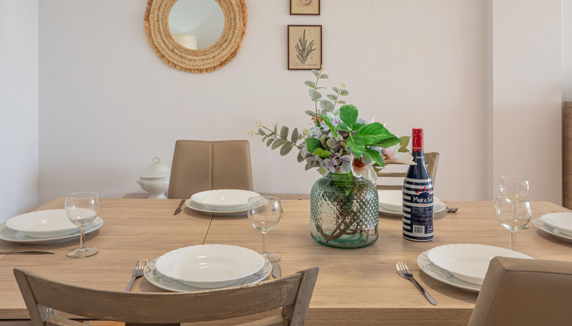 Una mesa de comedor preparada con platos, cubiertos y una botella de vino Mare Solo.