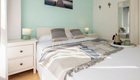 Une chambre à coucher avec un lit, des tables de chevet, une commode, une lampe, un miroir et un tableau accroché au mur.