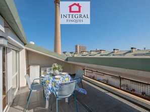 Un balcon avec une table dressée pour le repas, des chaises et un vase décoratif.