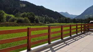 A wooden fence overlooking a green field and forested hills.