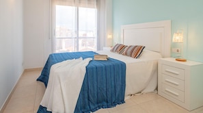 A bedroom with a bed, a bedside table, a lamp, and a window with curtains.