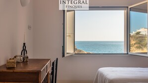 Une chambre avec une grande fenêtre donnant sur la mer. On y trouve un lit, un bureau avec une lampe et une petite table avec une bougie.