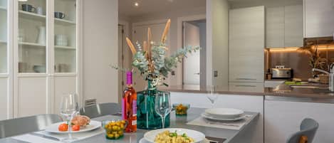 A modern kitchen with a dining area, featuring a table set for two with plates, glasses, and a bottle of wine.