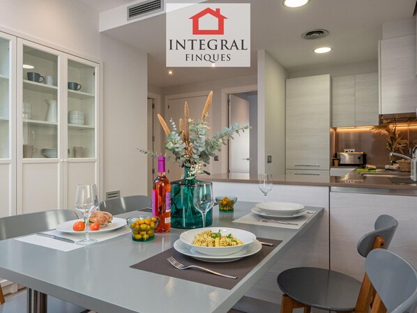 Une cuisine moderne avec un coin repas, comprenant une table mise pour deux personnes, avec assiettes, verres et une bouteille de vin.