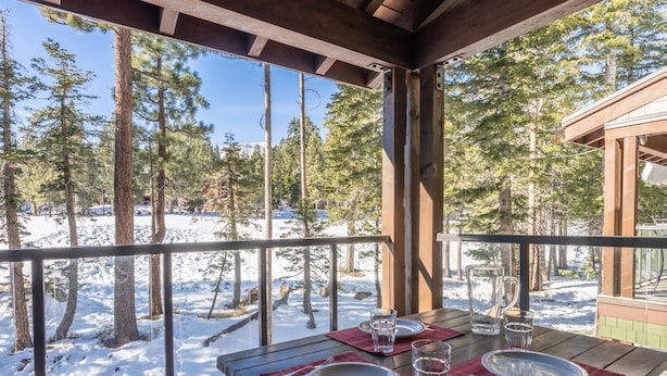 Une terrasse en bois avec une table dressée pour deux personnes, offrant une vue sur un paysage enneigé et des arbres.