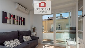 A modern living room with a grey sofa, patterned cushions, a small white side table with a vase, and a large sliding glass door leading to a balcony. - Stunning Duplex 200m from Platja Gran, 3BR, Balcony, Terrace, Parking, WiFi, A/C, Lift (Palamós)