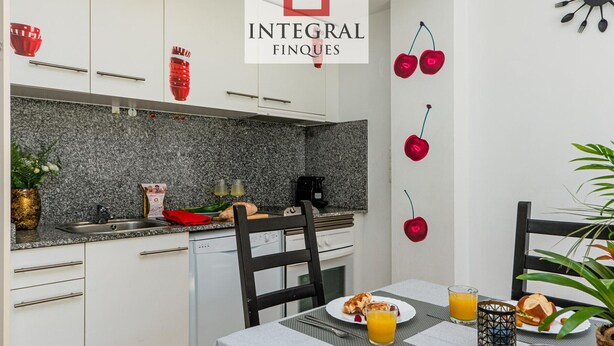 A modern kitchen with white cabinets, granite countertops, and a dining area with a table set for breakfast. - Stunning Duplex 200m from Platja Gran, 3BR, Balcony, Terrace, Parking, WiFi, A/C, Lift (Palamós)