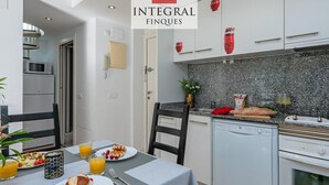 A modern kitchen with white cabinets, a granite countertop, and a built-in oven. There is a dining table with breakfast items and a chair. - Stunning Duplex 200m from Platja Gran, 3BR, Balcony, Terrace, Parking, WiFi, A/C, Lift (Palamós)