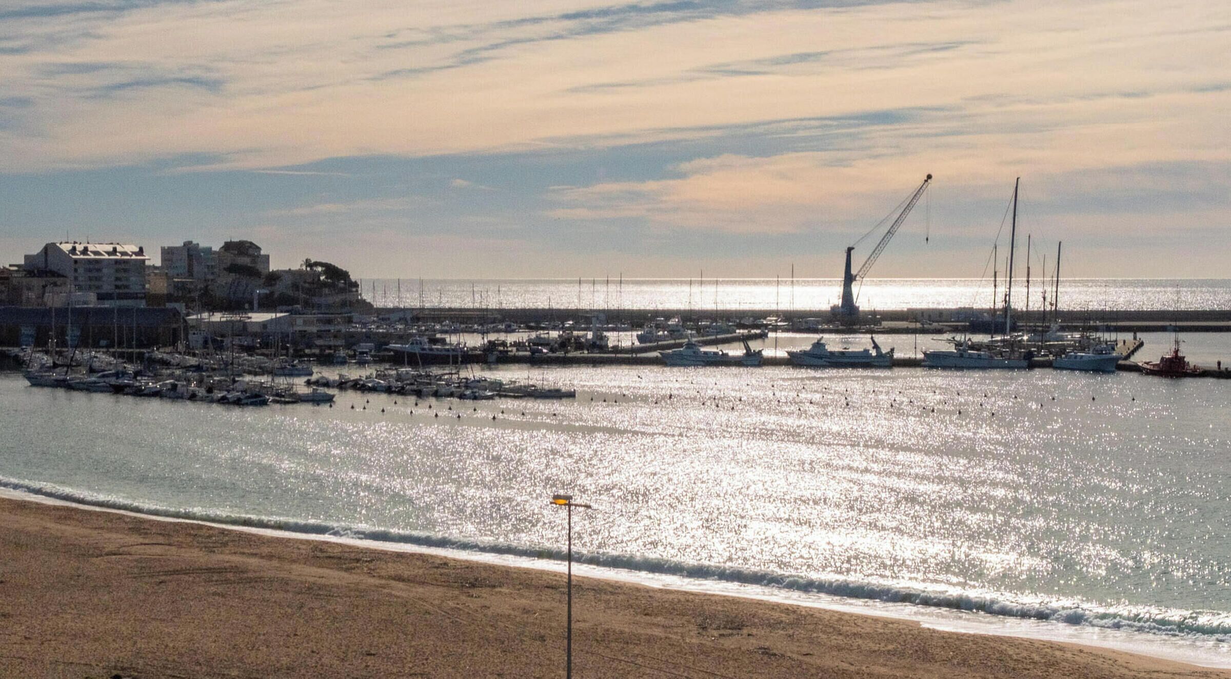 Un port de plaisance situé sur la côte, avec des bateaux amarrés, une jetée s’avançant dans l’eau et des bâtiments en arrière-plan.