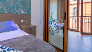 Een hotelkamer met een bed, een nachtkastje, een bureau en een schuifdeur die leidt naar een balkon met een stoel en een tafel.